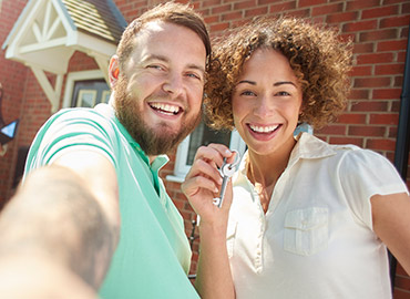 Couple taking selfie and holding up keys in front of new house.