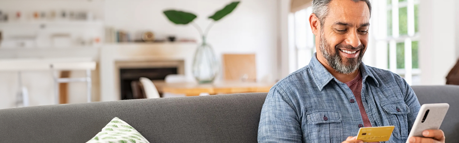A man smiling while holding his phone in one hand and a debit card in the other.