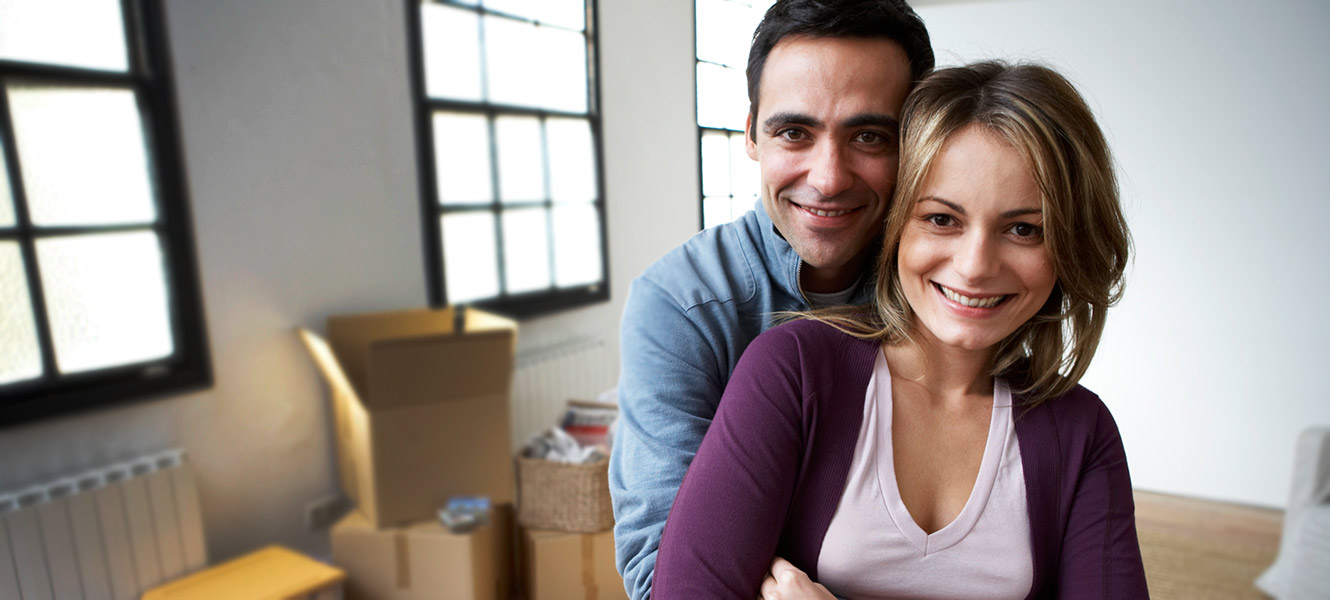 Couple embracing in new home with unpacked boxes in background.